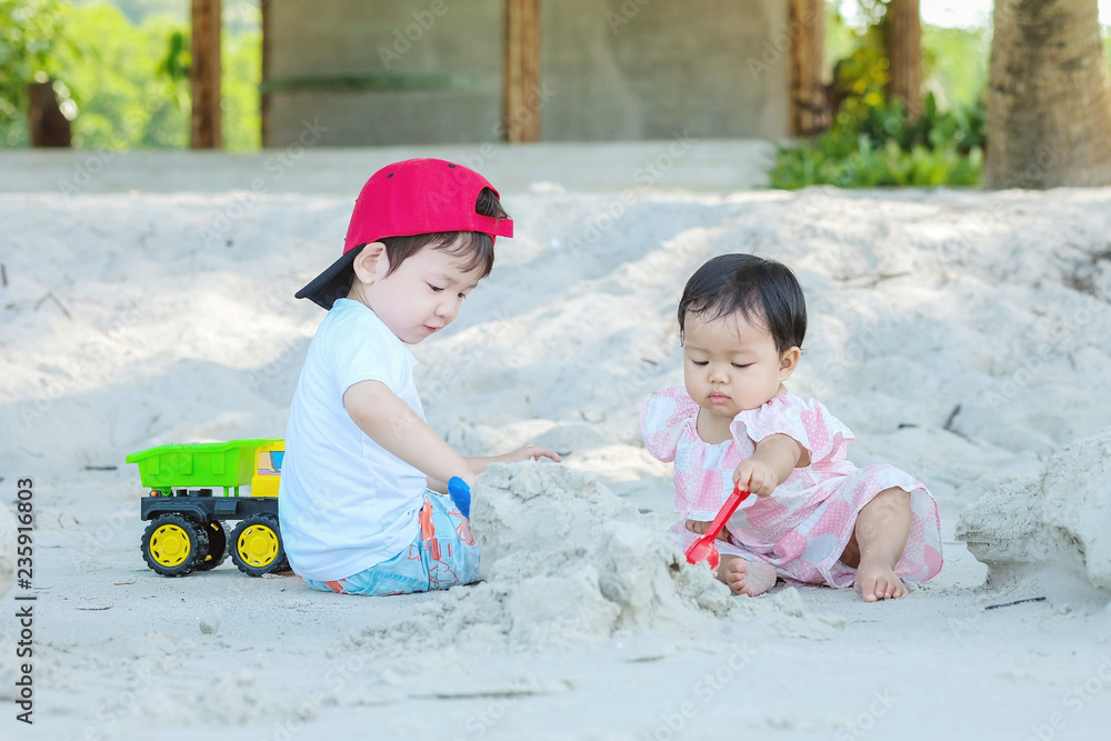 Closeup cute asian boy and girl play with sand and toy together on beach textured background Closeup cute asian boy and girl play with sand and toy together on beach textured background