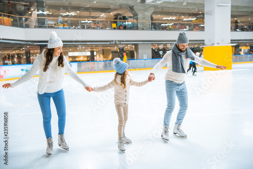 family in sweaters holding hands while skating together on ice rink