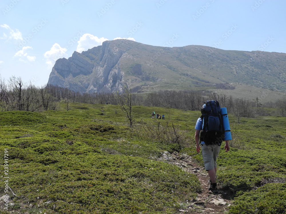 Beautiful mountain landscape. People with backpacks walking by hiking trail towards the mountain range.