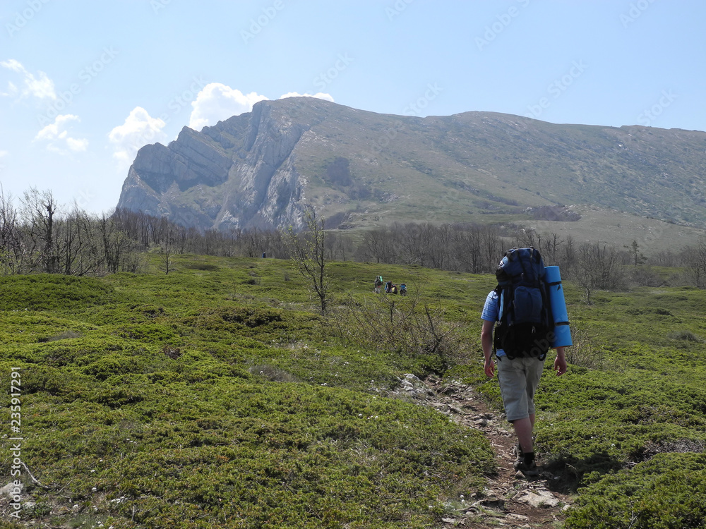 Beautiful mountain landscape. People with backpacks walking by hiking trail towards the mountain range. Beautiful mountain landscape. People with backpacks walking by hiking trail towards the mountain range.