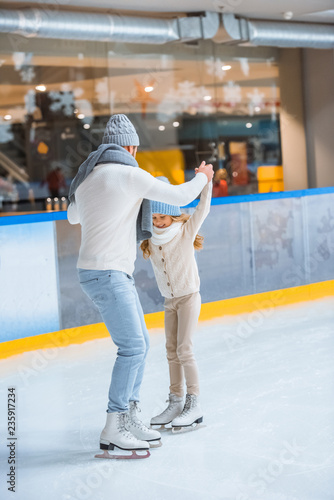 father and daughter in knitted sweaters skating on ice rink together