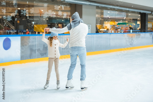 father and daughter holding hands while skating together on sakting rink