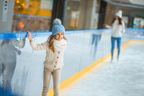 little child in knitted hat and sweater skating on ice rink