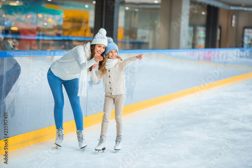 smiling mother and daughter pointing away on skating rink