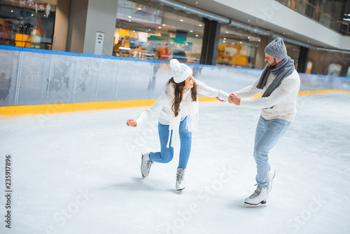 man teaching girlfriend how to skate on ice rink
