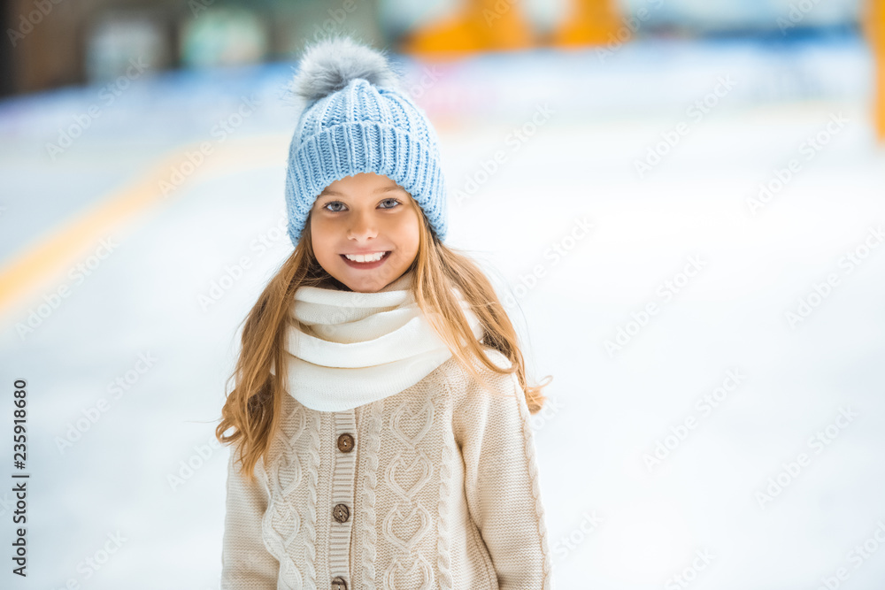 Obraz premium portrait of happy kid in knitted hat looking at camera on skating rink