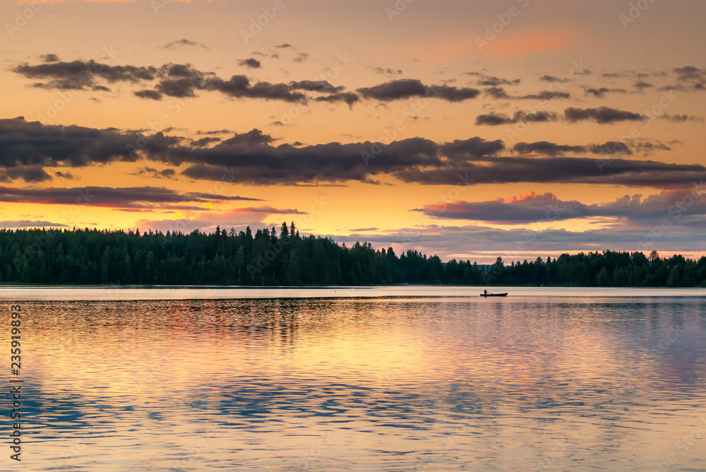 A lake in Finland during the midnight sun with orange-yellow reflections of the clouds in it. Photo taken August 2017 lake Ristijarvi, Finland.