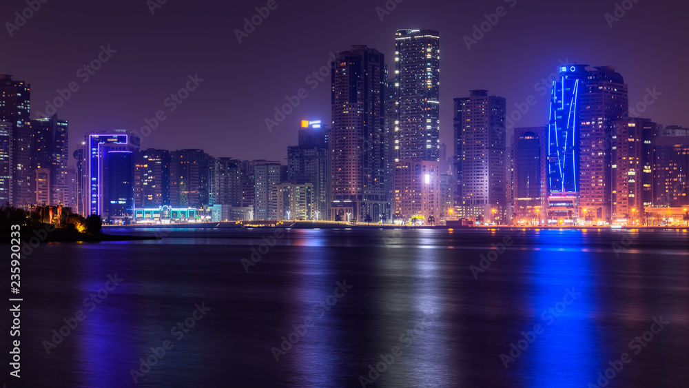 Fototapeta premium Beautiful view to Sharjah city center lights skyline at night, United Arab Emirates. Skyscrapers are reflecting in water