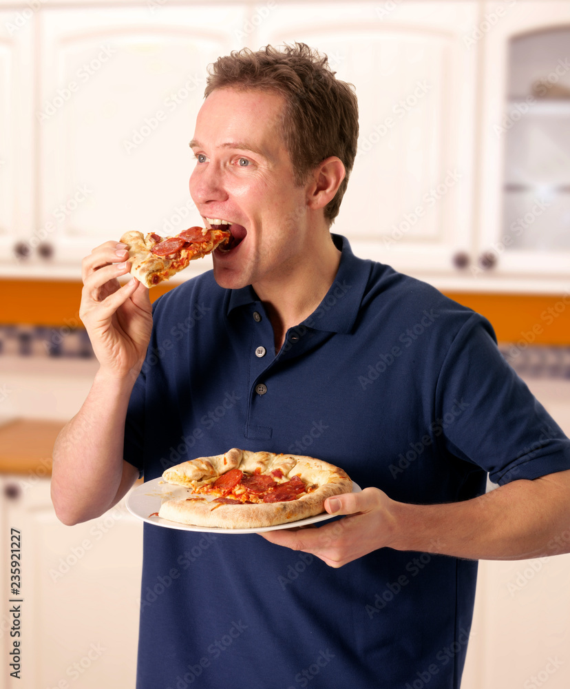 MAN IN KITCHEN EATING PIZZA