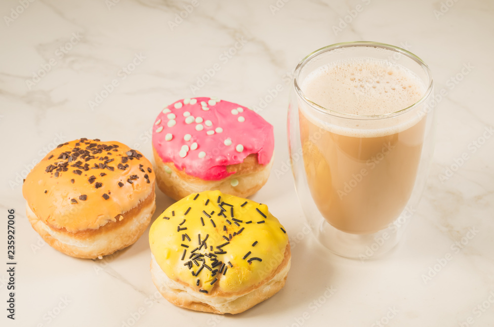 donuts in glazes and a glass of a cappuccino/donuts in glazes and a glass of a cappuccino on a white table. Selective focus donuts in glazes and a glass of a cappuccino/donuts in glazes and a glass of a cappuccino on a white table. Selective focus