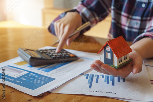 Woman holding house model in hand and calculating financial chart for investment to buying property.