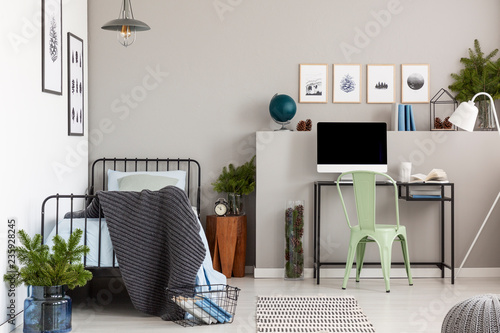 Grey elegant bedroom with single metal bed with blue bedding and dark grey blanket next to home office in teenager bedroom