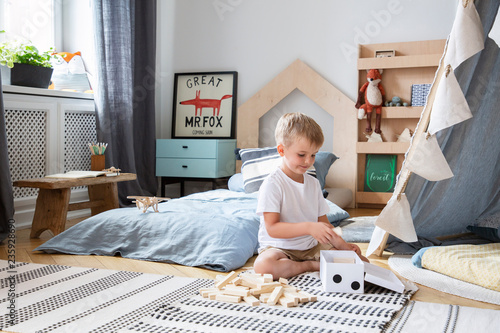Cute little boy playing with wooden blocks in stylish bedroom with scandinavian design, real photo