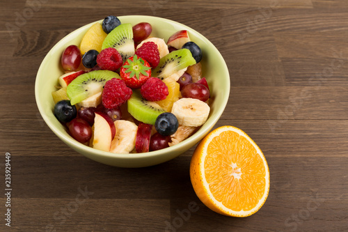 Fruit Salad in Green Bowl and a slice of orange on wooden Table, Top View. copy space.