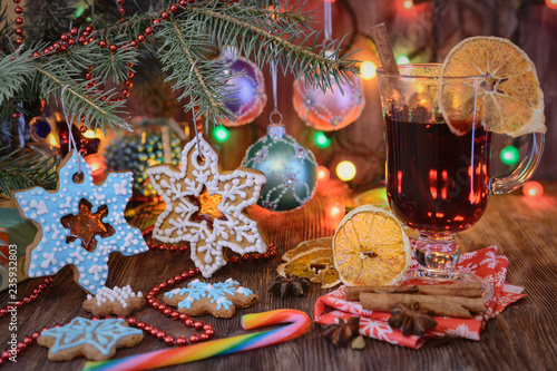 Christmas gingerbread shaped snowflakes as Christmas-tree decorations hang on Christmas-tree branches next to balls and glass of mulled wine in the light of the Christmas lights in the background