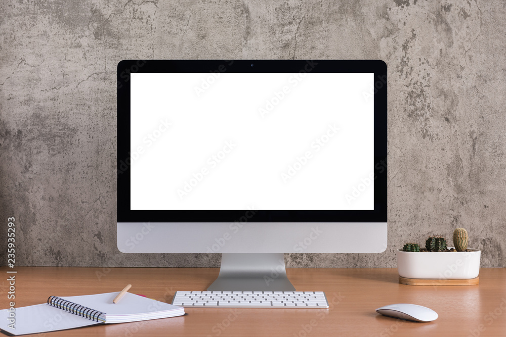 Blank screen of all in one computer with note book, pencil and cactus vase on raw concrete background Blank screen of all in one computer with note book, pencil and cactus vase on raw concrete background