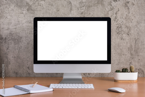 Blank screen of all in one computer with note book, pencil and cactus vase on raw concrete background