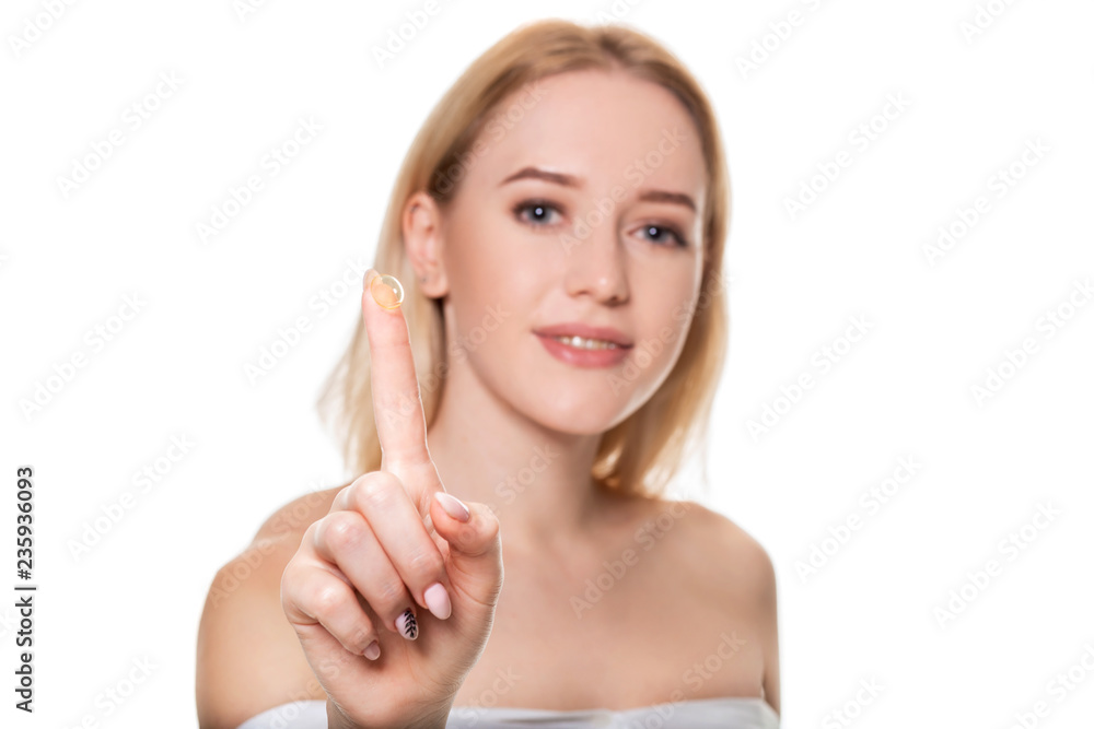 Focus on contact lens on finger of young woman. Young woman holding contact lens on finger in front of her face. Woman holding contact lens on white background.