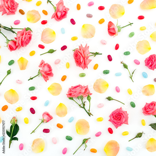 Roses flowers and petals with bright sugar candy on white background. Flat lay, top view.