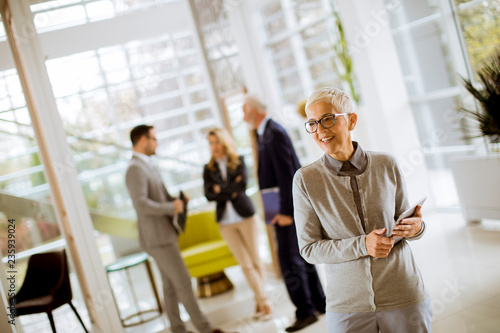 Portrait of senior businesswoman with digital tablet while other business people standing in background