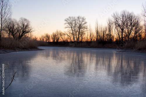 Beautiful landscape of forest lake in the early morning. Frozen lake in the forest. The reflection on the ice.