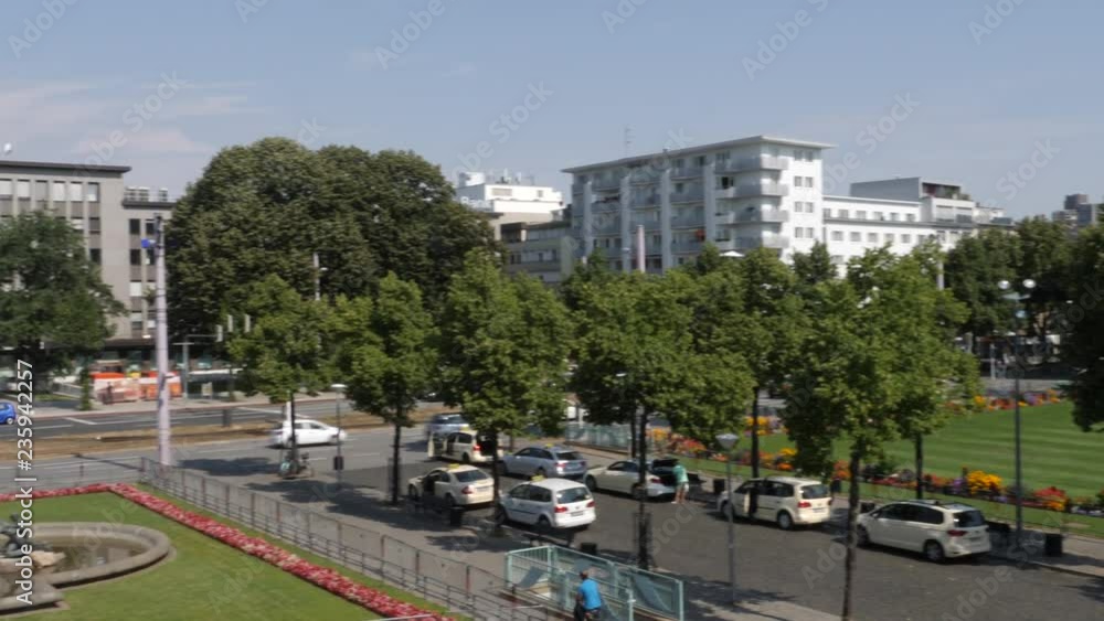 Camera pans left across a grassy park area to the square with the Triton Fountain. City streets and buildings are in the background. Camera pans left across a grassy park area to the square with the Triton Fountain. City streets and buildings are in the background.
