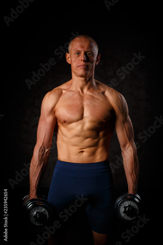 Handsome muscular man working out with dumbbells over black background.