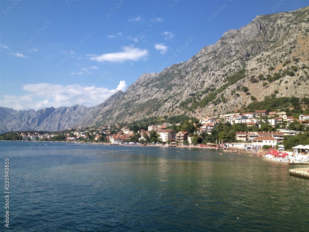 Montenegro coast near Sutomore, naked mountains and hills showing in the background, with houses, hotels and beach in the midground and calm sea surface in the foreground. 