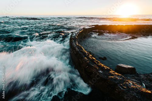 Ocean waves crashing against barrier at sunset photo