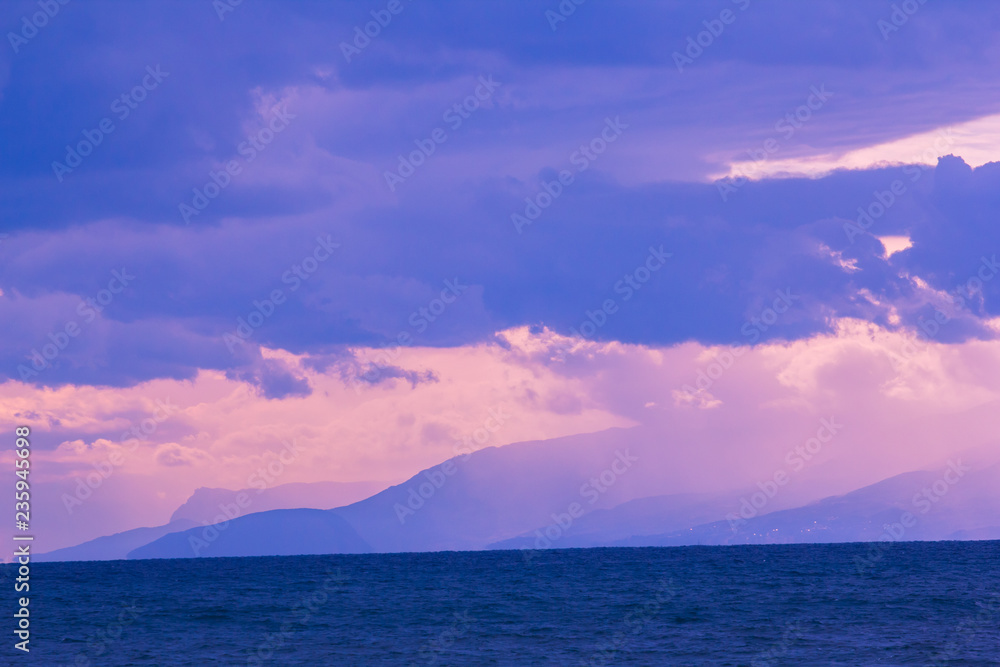 seascape of sunset purple sky with clouds and sea open water with mountains in background