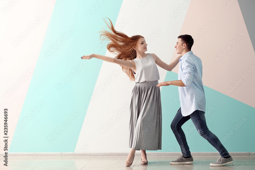 Cute young couple dancing against color wall
