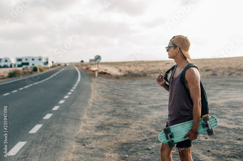 Young hipster guy with skateboard and backpack, standing on a asphalt roadside.