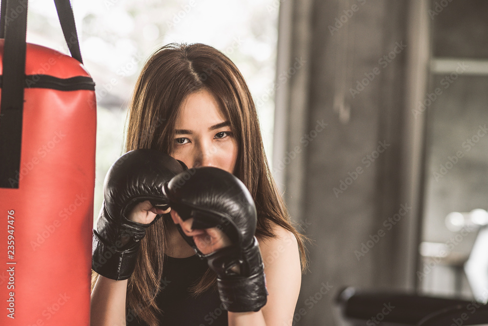 Attractive female boxer training with kick boxing at gym with blackgloves.