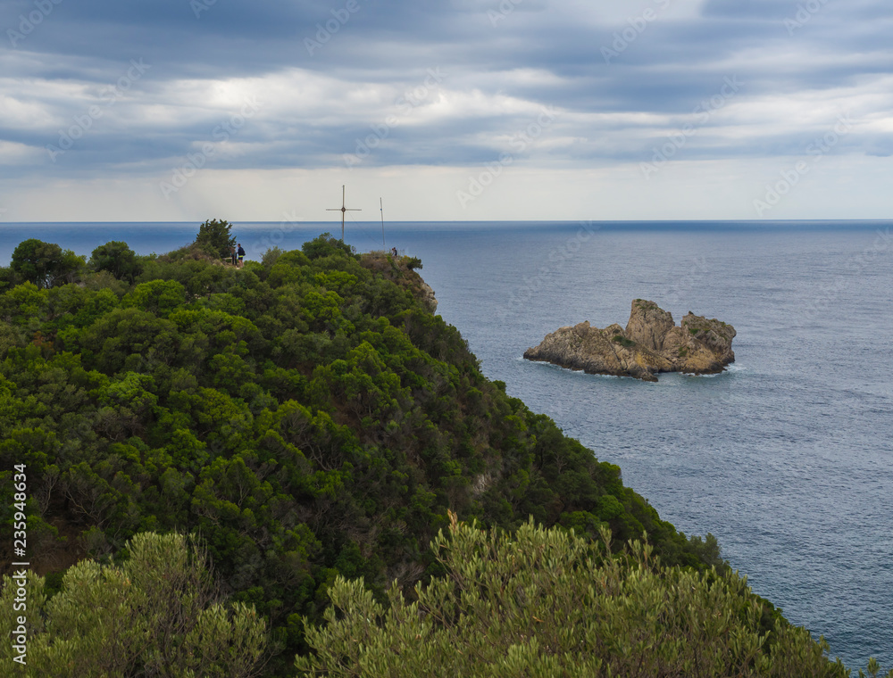 View point with cross and cllifs, trees and green hill at Paleokastritsa bay, summer cloudy sky, Corfu, Kerkyra, Greece