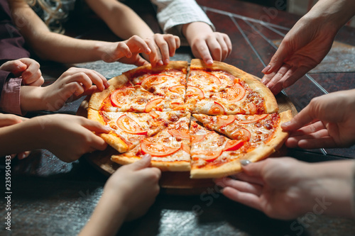 Hands taking pizza slices from wooden table, close up view.