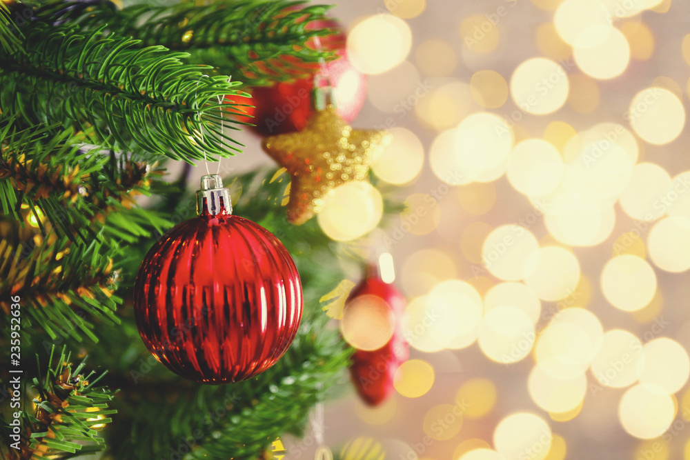 Fototapeta premium Decorated Christmas tree on soft yellow lights with bokeh effect background. Festive composition with fir and blurry sparkling backdrop, new year holiday decorations. Close up, copy space.