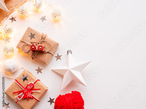Christmas and New Year wrapped DIY presents in craft paper. Gift tied with rustic thread with toy train as decoration. Metal light bulbs with delicate pattern. Christmas tree decorations.