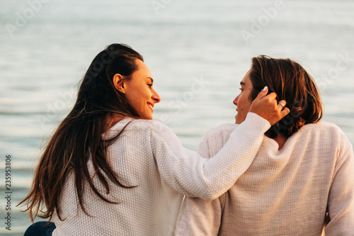 Young woman with hand on hairs of man sitting near water photo