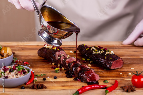 Fotografi The cook waters venison meat with juniper sauce with nuts