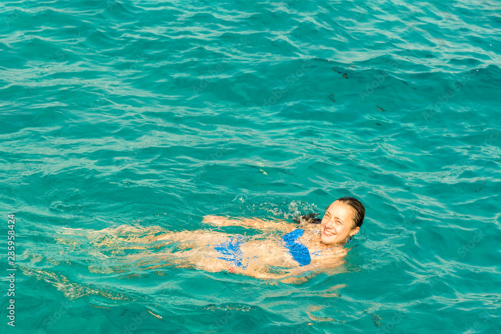 Young woman smiles, swiming in ocean. Young woman in bikini swimming in clear water.