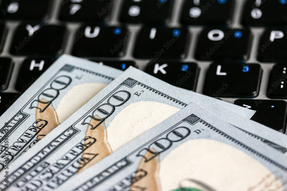 Closeup view of one hundred dollar banknotes lying on the laptop keyboard. Closeup view of one hundred dollar banknotes lying on the laptop keyboard.