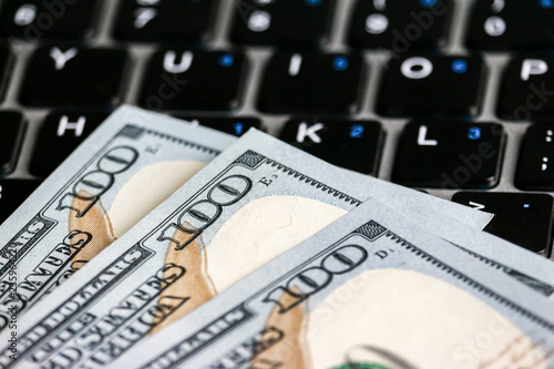 Closeup view of one hundred dollar banknotes lying on the laptop keyboard.