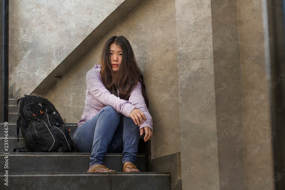 depressed Asian Korean student woman or bullied teenager sitting outdoors on street staircase overwhelmed and anxious feeling desperate suffering depression