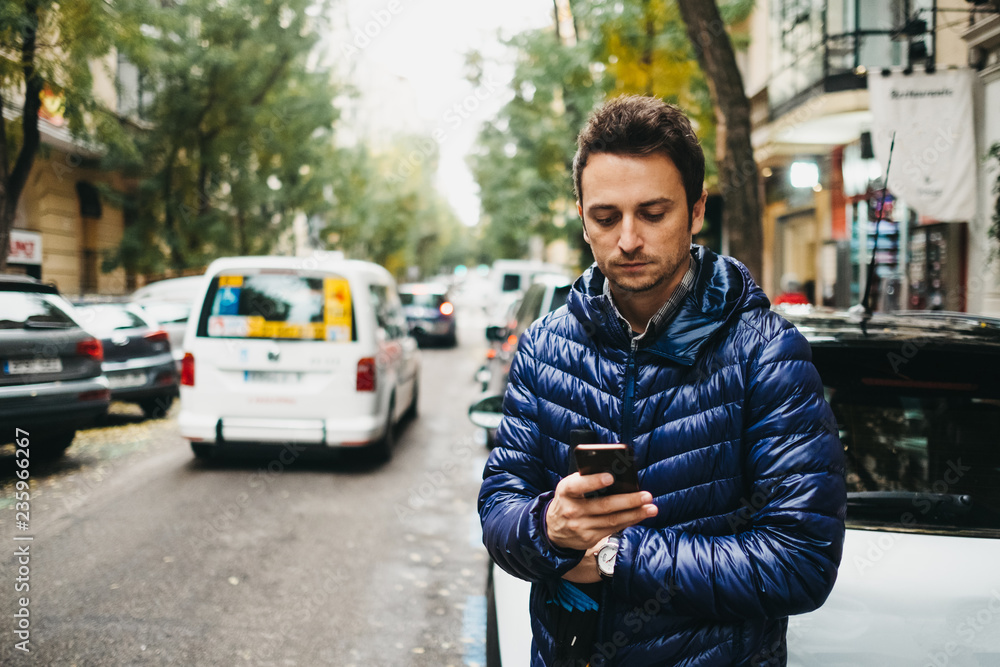 Young man with smartphone near cars on street Young man with smartphone near cars on street