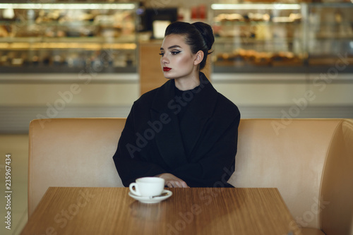 Beautiful thoughtful lady with perfect make up and hair scraped back into a high bun sitting alone in the nice cafe drinking coffee. Text space