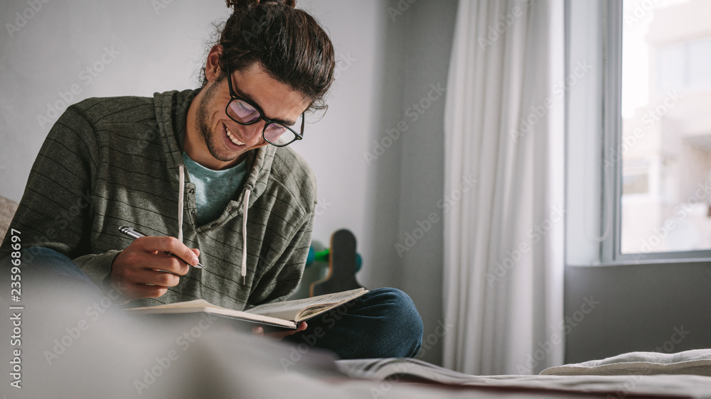 Smiling student studying for exam sitting on bed Smiling student studying for exam sitting on bed