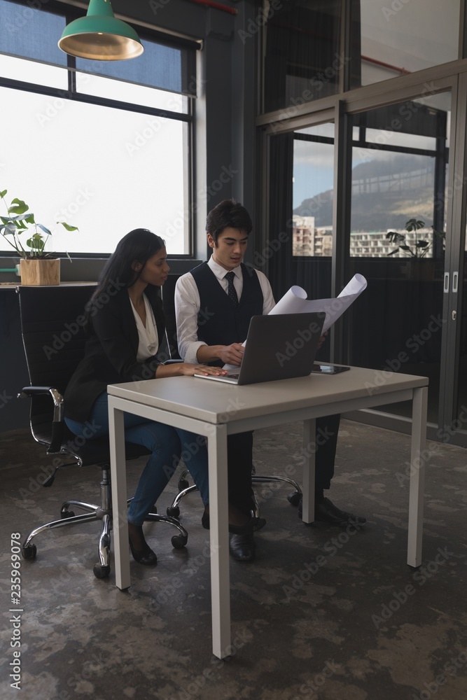 Executives discussing over blue print while using laptop Executives discussing over blue print while using laptop