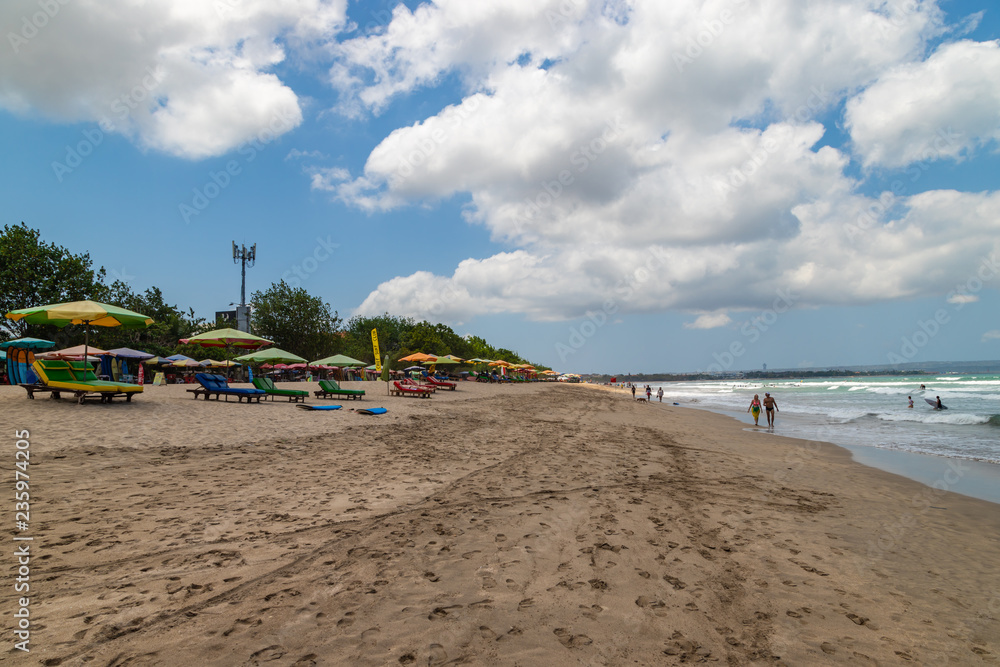 KUTA, BALI, INDONESIA - OCTOBER 22, 2018: Reclining chairs with sun umbrellas on the beach with some people relaxing on them.