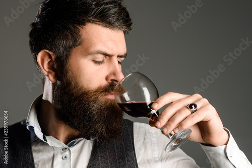 Berded man tasting glass of wine. Winetasting and degustation concept. New year party. Serious man drinking red wine. Sommelier tasting red wine. Man in waistcoat drink glass of red wine. Closeup.