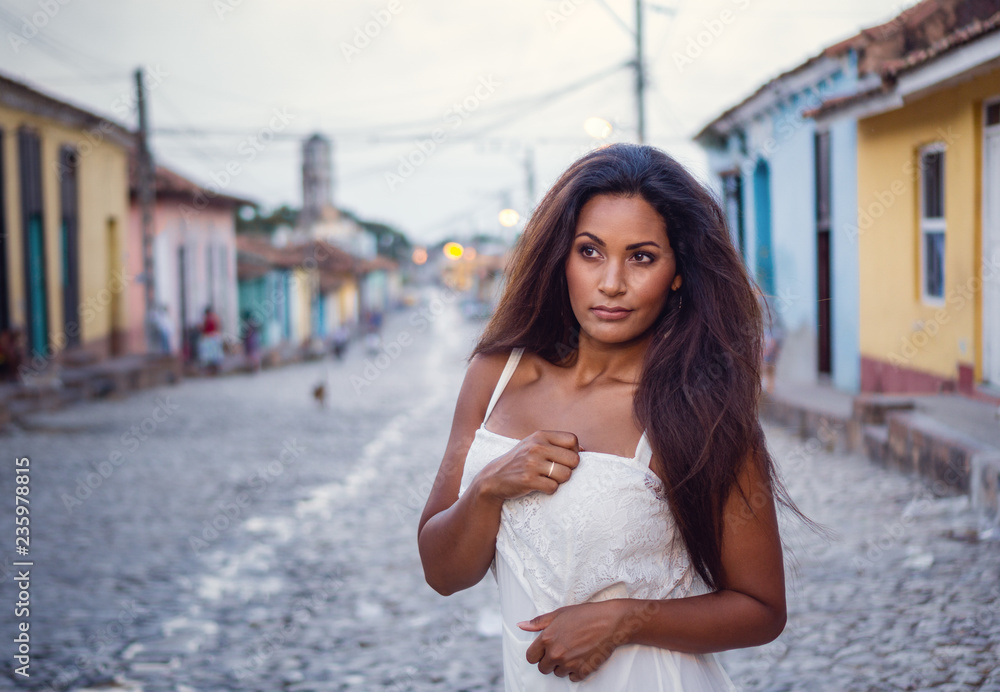Beautiful dark skinned young lady in white dress wearing a wedding ring  standing in the old streets of Trinidad in Cuba.
